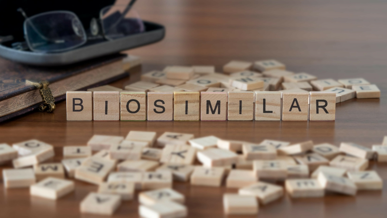 biosimilar word or concept represented by wooden letter tiles on a wooden table with glasses and a book. Image Credit: Adobe Stock Images/lexiconimages