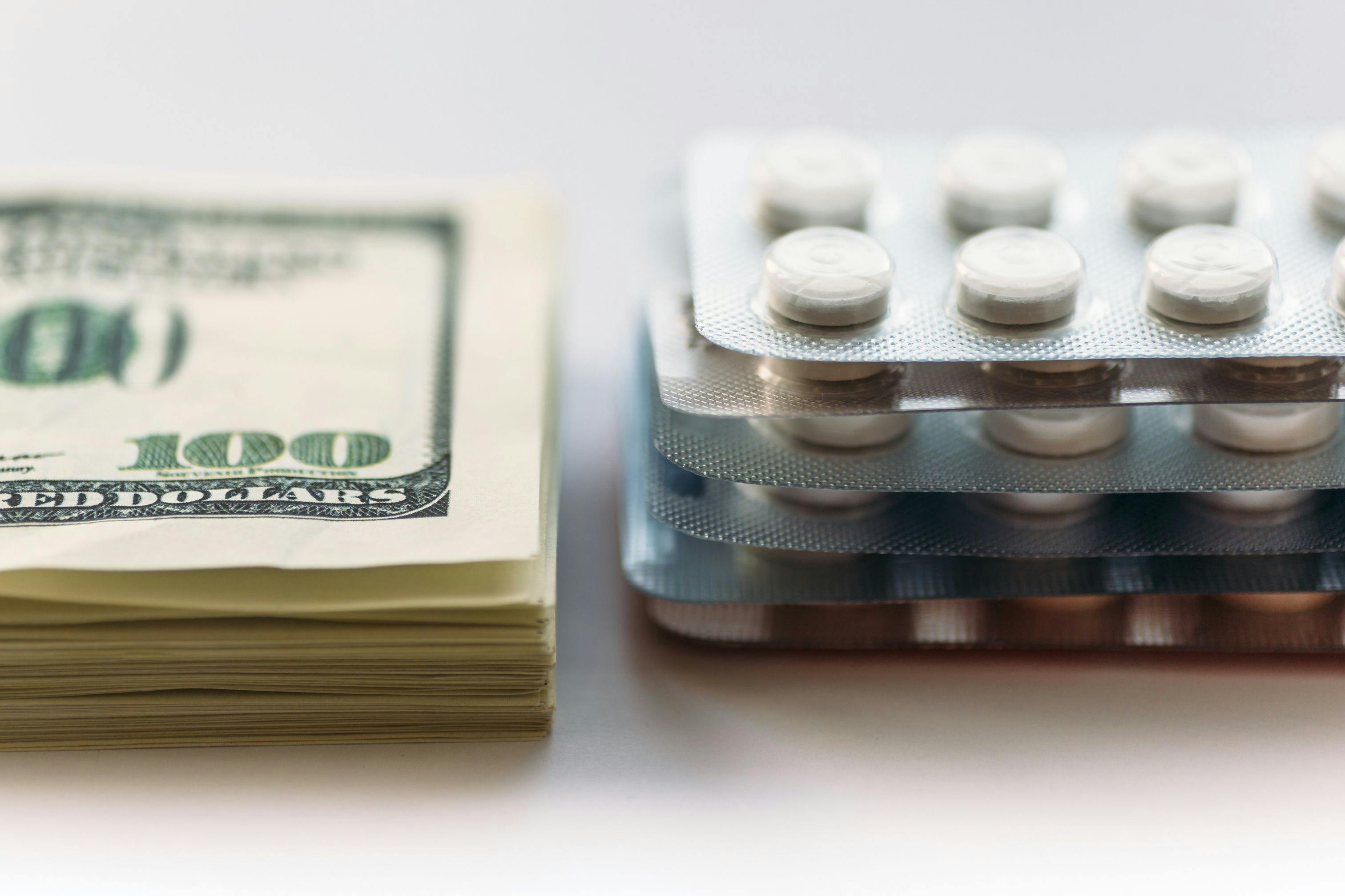 Image credit: DedMityay | stock.adobe.com. Bundle of money and pack of medication tablets or drug pills, close-up. Expensive health care concept